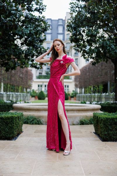 Rochie STRONG FLOWER lunga, fara maneci, cu decolteu, cu slit lung in partea din fata, pe un picior, din material elastic fuchsia metalizat, cu un trandafir si frunze lucrate manual, in mijloc cu cristale multicolore, aplicate in zona bustului 