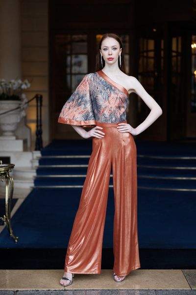 Salopeta STRONG LIQUID pe un umar, cu o maneca lunga, cu pantaloni lungi si largi, in partea de sus din jacquard cu cupru metalizat, gri metalizat si negru metalizat, model pene pauni, si in partea de jos din tesatura elastica cu pelicula lucioasa cupru